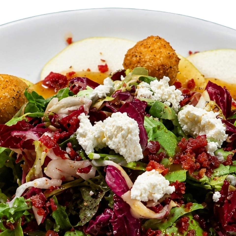 A fresh salad with mixed greens, crumbled cheese, bacon bits, fried balls, and pear slices.