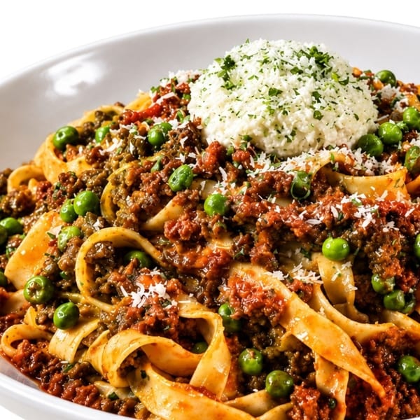 Close-up of pasta with meat sauce, green peas, and a dollop of ricotta cheese.