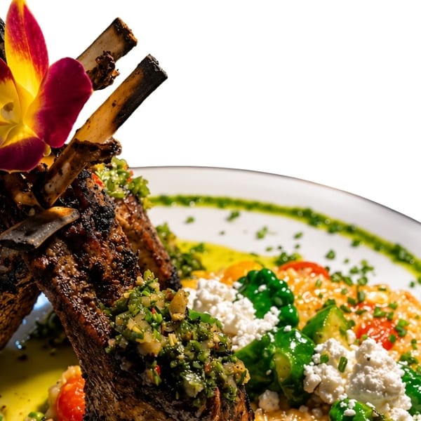 Grilled lamb chops with chimichurri, risotto, feta, and vegetables, garnished with an orchid.