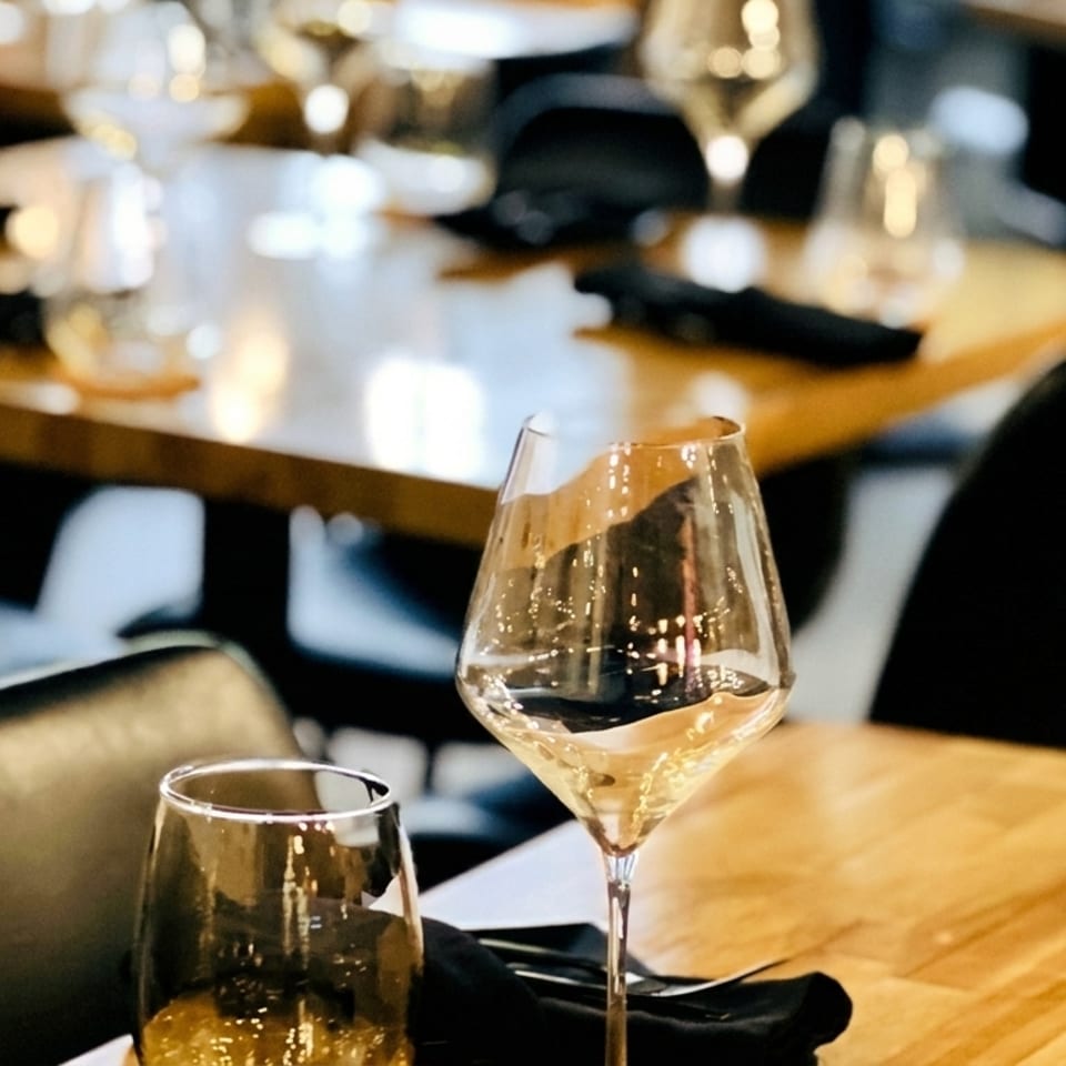 Wine glasses and place settings on wooden tables in a dimly lit restaurant dining room.