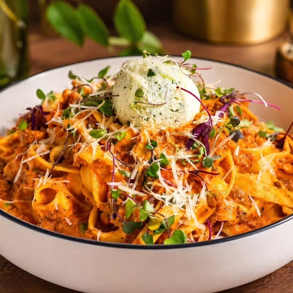 Pasta with red sauce, grated cheese, microgreens, and a scoop of ricotta in a white bowl.